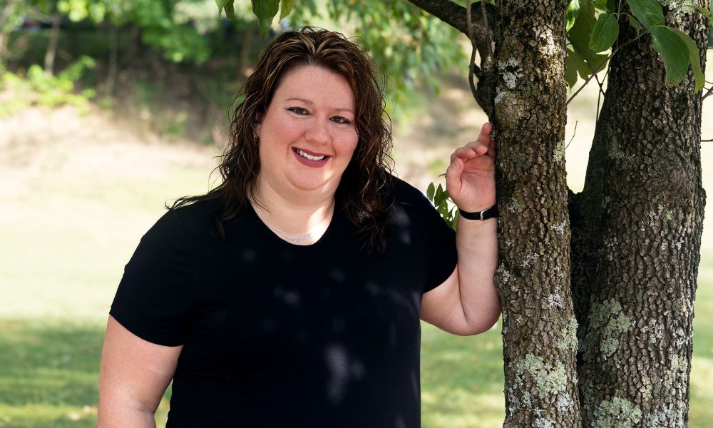 Nicole DeArmitt leaning against a tree, posing for camera.